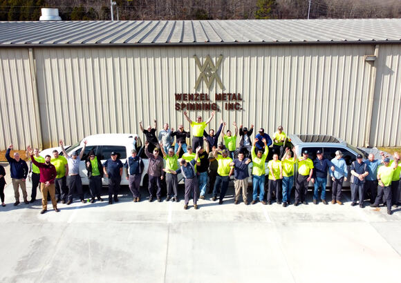 Large group of people waving in front of Wenzel Metal Spinning building.